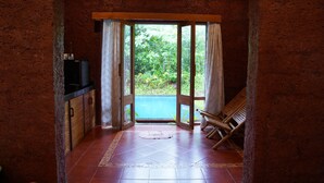 A room with a kitchen area, a wooden chair, and a view of greenery through a glass door. - Forest Escapes Koyna (Patan)