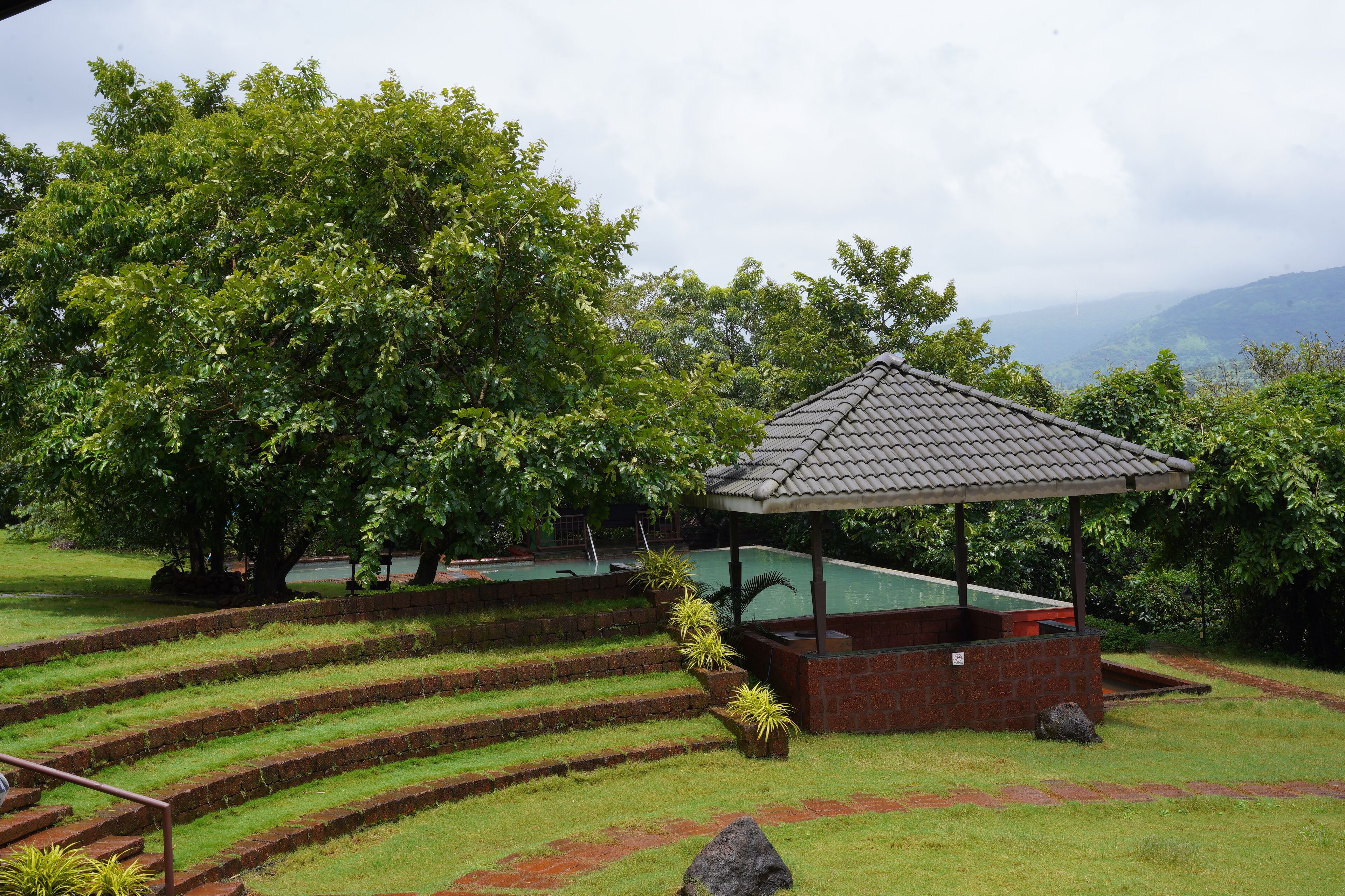 A gazebo with a tiled roof, surrounded by a brick wall and steps leading up to it.