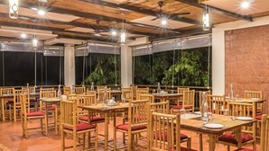 A restaurant with wooden tables and chairs, a brick wall, and hanging lights. - Forest Escapes Koyna (Patan)