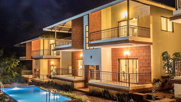 A multi-story hotel with a swimming pool, balconies, and warm lighting. - Forest Escapes Koyna (Patan)