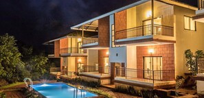 A multi-story hotel with a swimming pool, balconies, and warm lighting. - Forest Escapes Koyna (Patan)