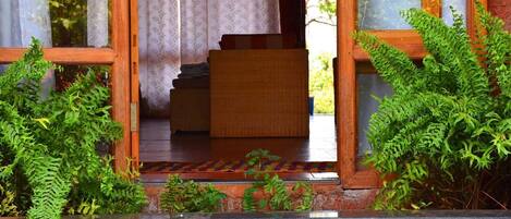 A wooden staircase leading to a room with a patterned rug, surrounded by lush green plants.