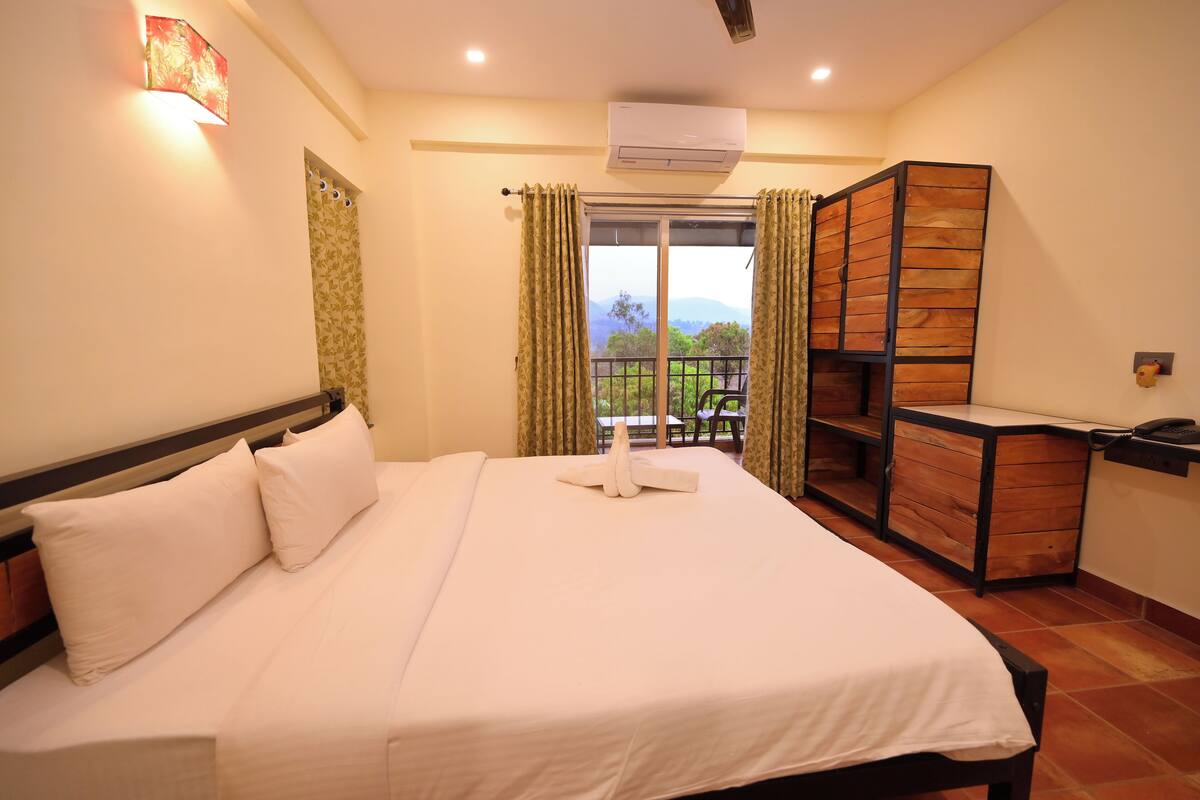 A hotel room with a large bed, a wooden desk, and a balcony with a view.