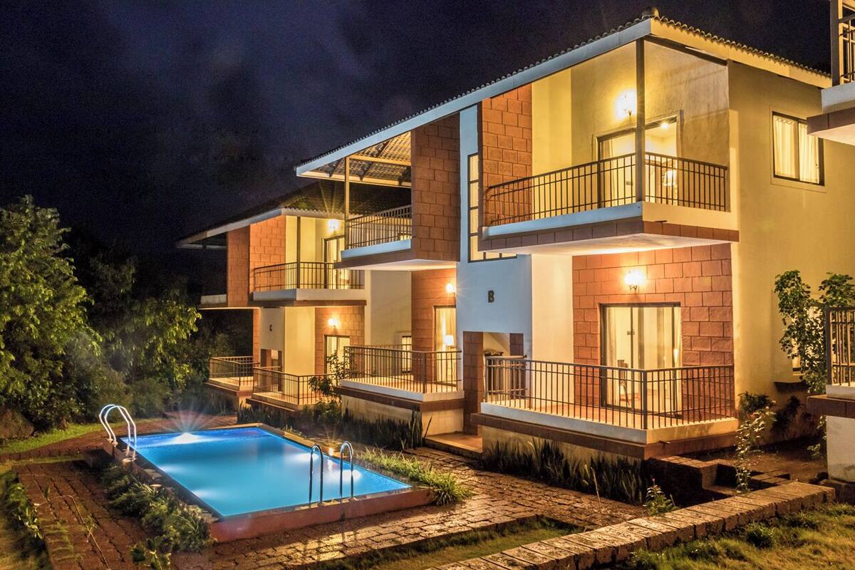 A modern two-story building with a swimming pool, balconies, and a well-lit exterior.