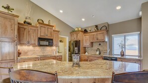 A spacious kitchen with granite countertops, wooden cabinets, and a large island with bar stools. - TexCo (Colorado Springs)