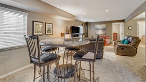 A spacious living room with a round glass table surrounded by chairs, a leather sofa, and a flat-screen TV mounted on the wall. - TexCo (Colorado Springs)