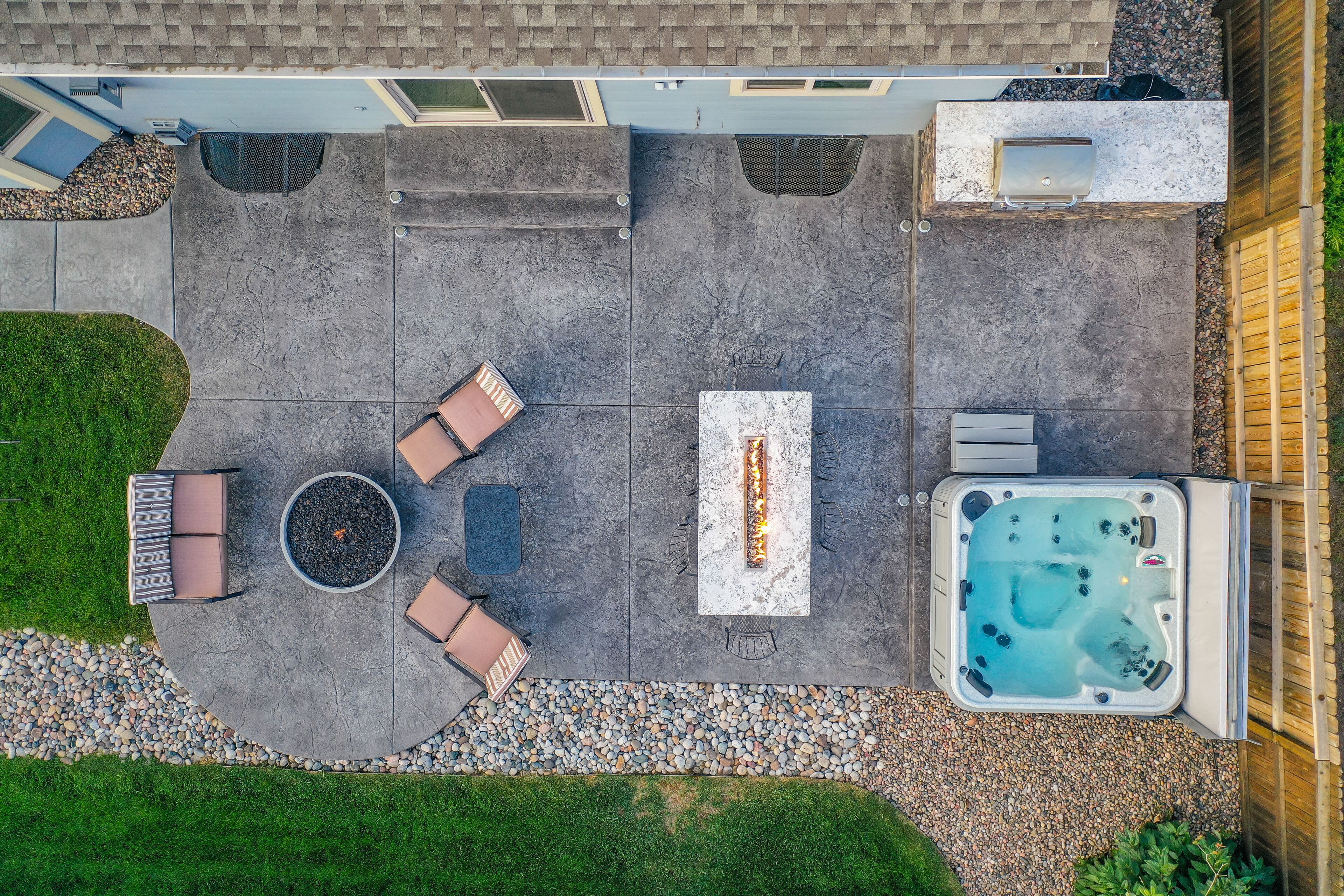 An aerial view of a patio with a fire pit, seating area, and hot tub.