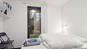 A bedroom with a bed, a chair, a bookshelf, and a window with curtains.