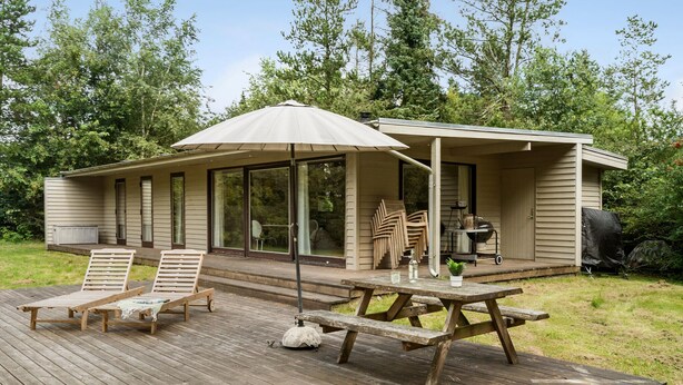 A wooden deck with lounge chairs and a picnic table, overlooking a forested area.