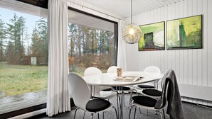 A modern dining area with a round table and chairs, large windows with curtains, and abstract art on the wall.