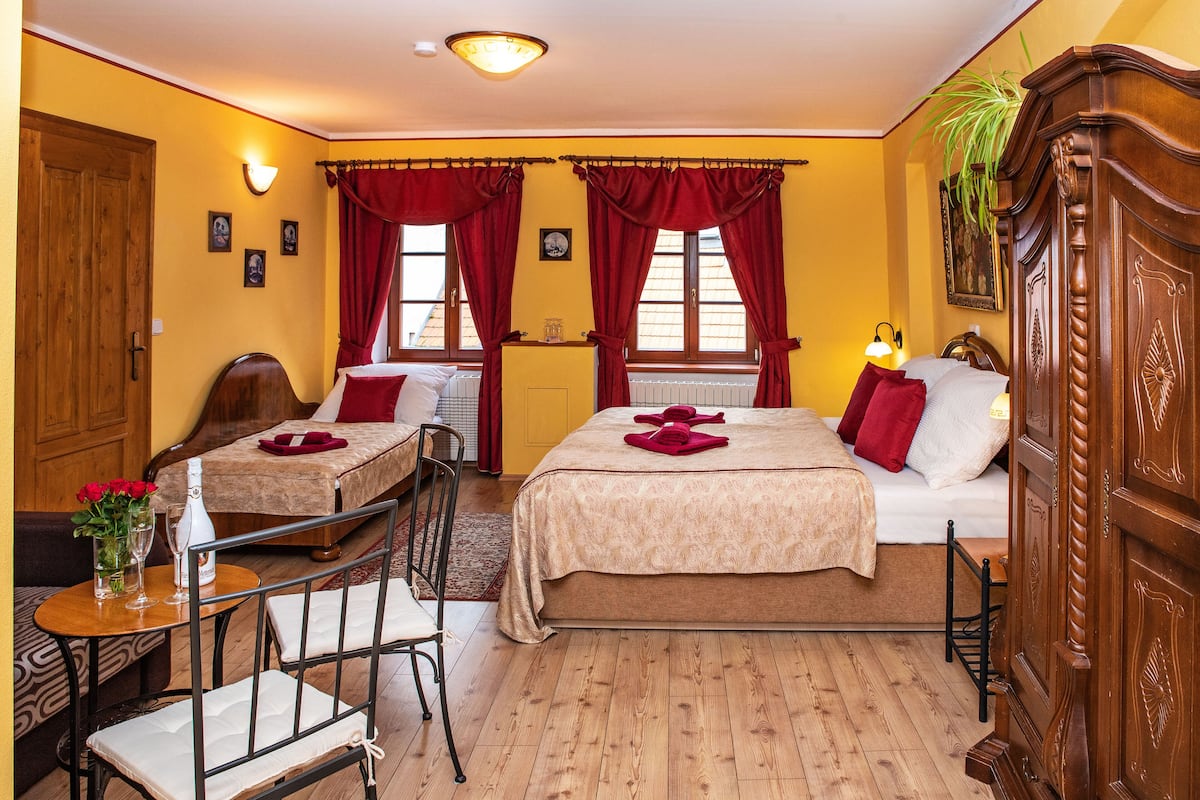 A hotel room with two beds, a wooden floor, a dining table with chairs, and a small table with a vase of flowers.