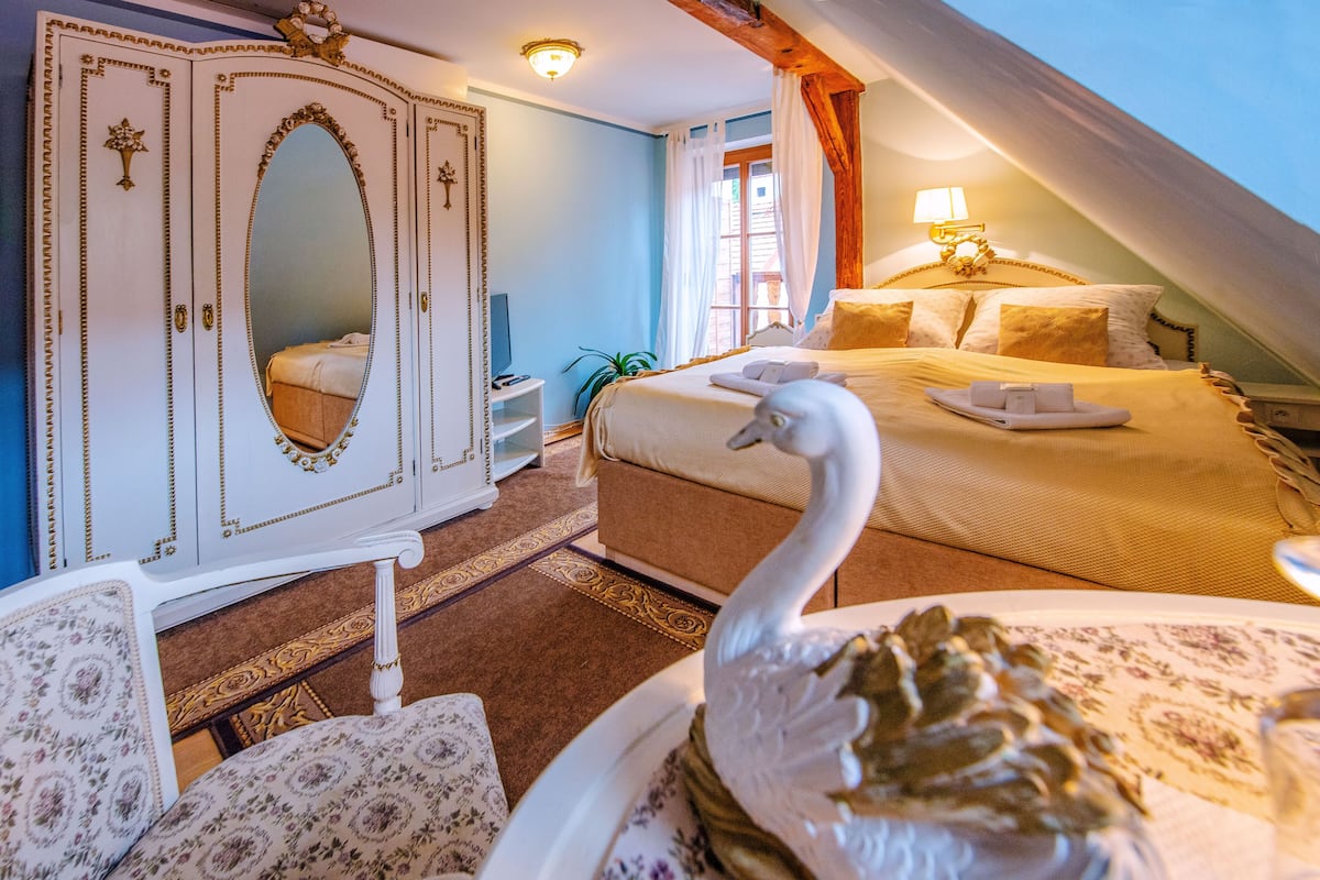 A bedroom with a bed, a dresser, a mirror, a swan statue, and a window with curtains.
