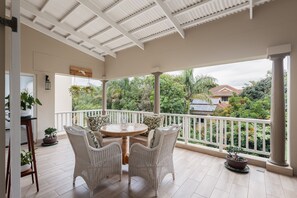 A covered balcony with wicker furniture, a round table, and potted plants. - 63 Villa Med Ballito (Dolphin Coast)