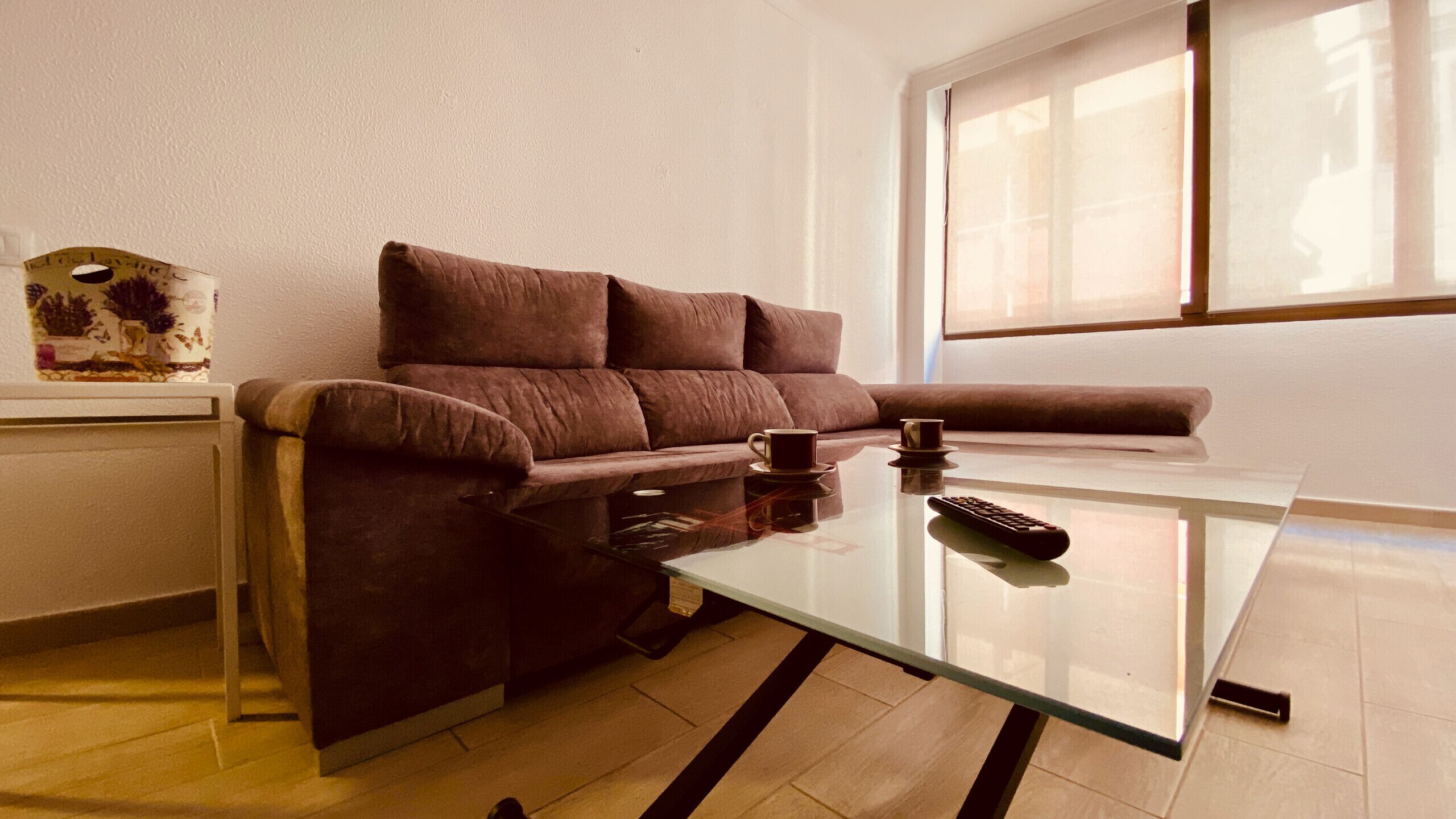 Una sala de estar moderna con un sofá marrón, una mesa de centro de vidrio y un control remoto.