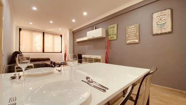A dining area with a white table set for four, including plates, cutlery, and glasses. There are two wall-mounted signs with motivational quotes.