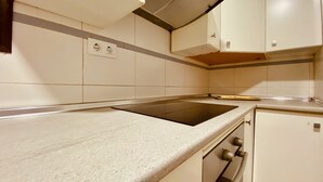 A kitchen with a black induction cooktop, white cabinets, and a small refrigerator.