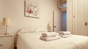 A neatly made bed with folded towels, a bedside lamp, and a wall art piece.
