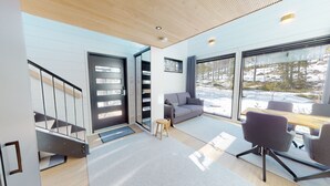 A modern interior with a staircase, grey sofa, and a dining area with a view of a snowy landscape.