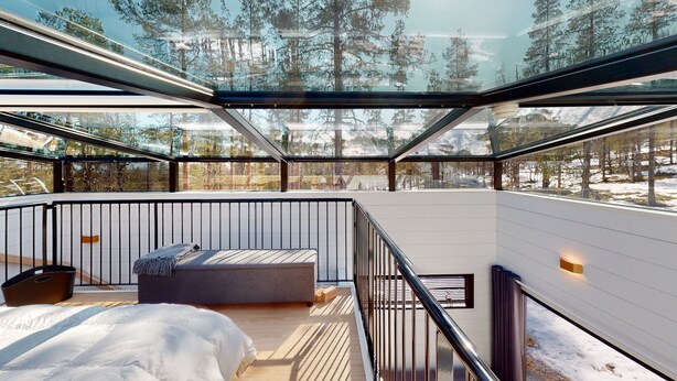 A modern interior with a glass ceiling, wooden flooring, a bed, and a seating area.