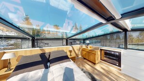 A modern room with a skylight, wooden furniture, a fireplace, and a view of trees and buildings.