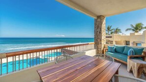 A balcony with a wooden table and chairs, a stone pillar, a sofa with teal cushions, and a view of the ocean. - Soleado 312 Oceanfront Condo at Costa Azul Beach! (San José del Cabo)