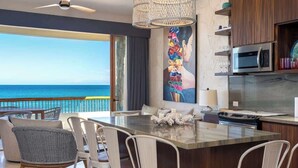 A modern kitchen with a large island, a dining area with chairs, a view of the ocean, and a ceiling fan. - Soleado 312 Oceanfront Condo at Costa Azul Beach! (San José del Cabo)