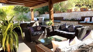 An outdoor patio area with wicker furniture, a glass table, and potted plants.