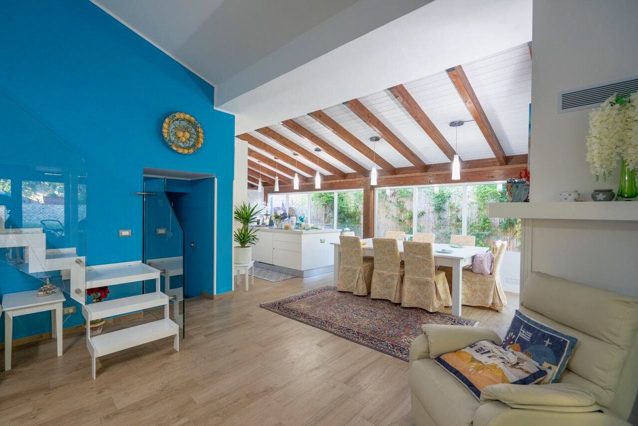 Amplia sala de estar con una pared azul de acento, vigas de madera, comedor con sillas y un sofá.