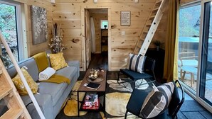 A cozy cabin interior with a loft bedroom, a living area with a sofa and coffee table, and a dining area with chairs. - Whispering Woods • Modern Cabin w/ HOT TUB (Stanton)
