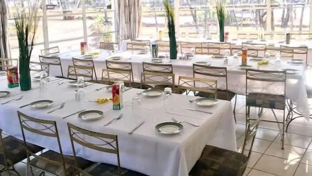 A dining area with tables set for four, each with white tablecloths, metal chairs, and basic tableware. - Cheltenham Park Resort  (Harare)