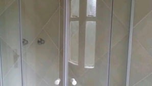 A glass-enclosed shower with a curved design, a visible showerhead, and a tiled floor. - Cheltenham Park Resort  (Harare)