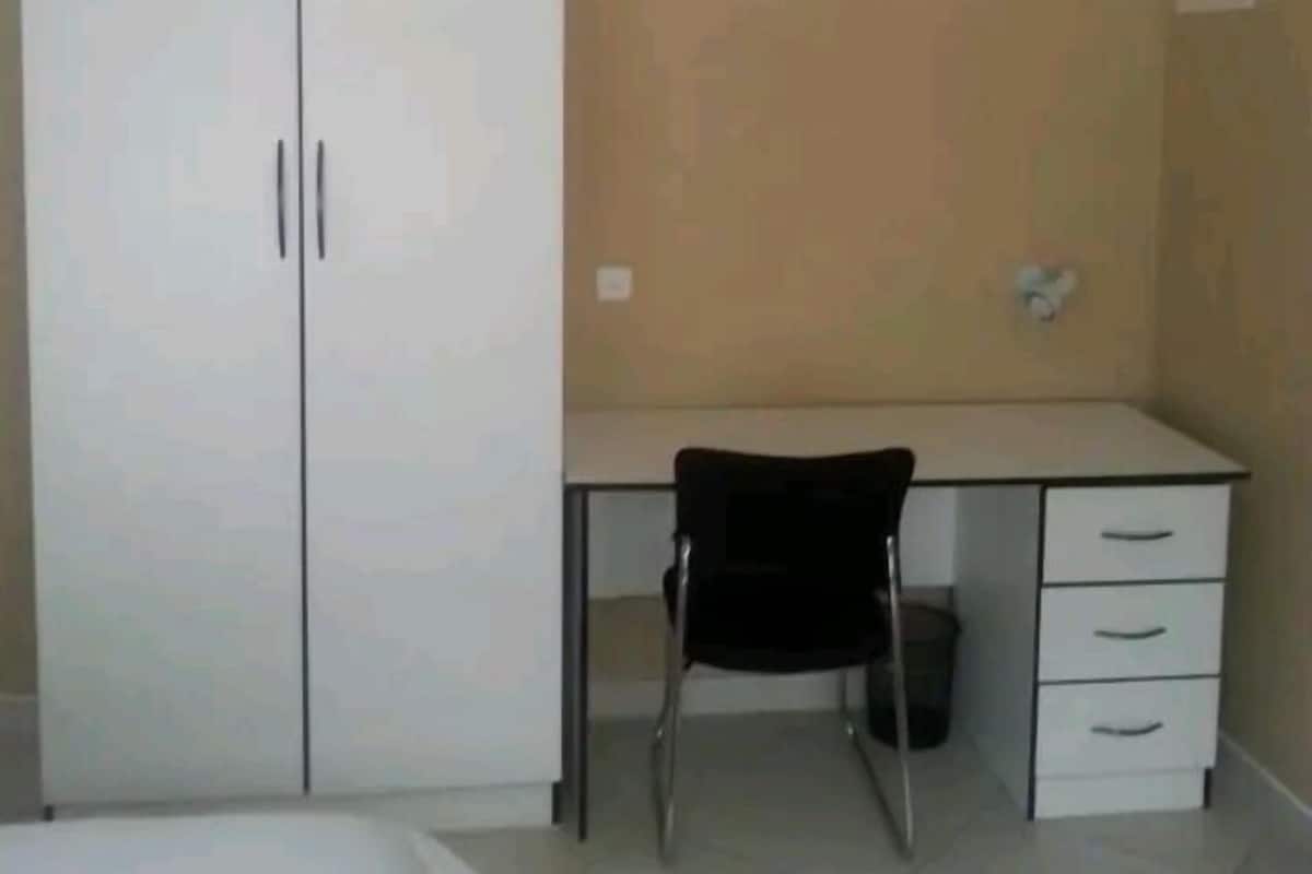A bedroom with a double wardrobe, a desk with a chair, and a bed.
