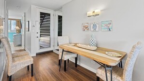 A dining area with a wooden table, wicker chairs, and wall-mounted light fixtures. - Oceanfront Beachfront Escape Hale Kai 1Bed (Lahaina)
