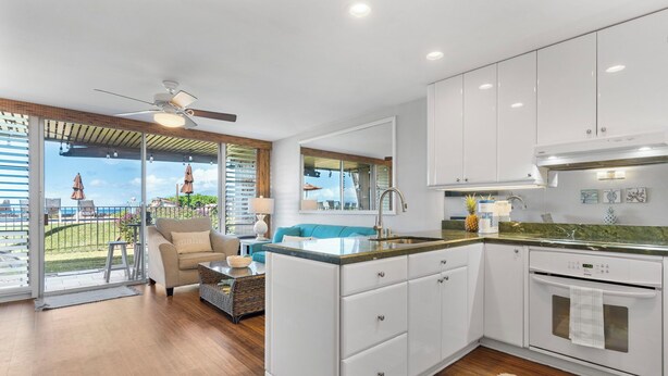 A modern kitchen with white cabinets, a central island, and a view of the outdoors. - Oceanfront Beachfront Escape Hale Kai 1Bed (Lahaina)