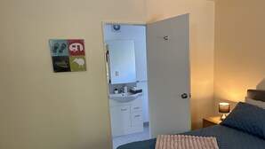 Un dormitorio con cama, lámpara de noche, puerta que da a un baño y un detalle decorativo en la pared.