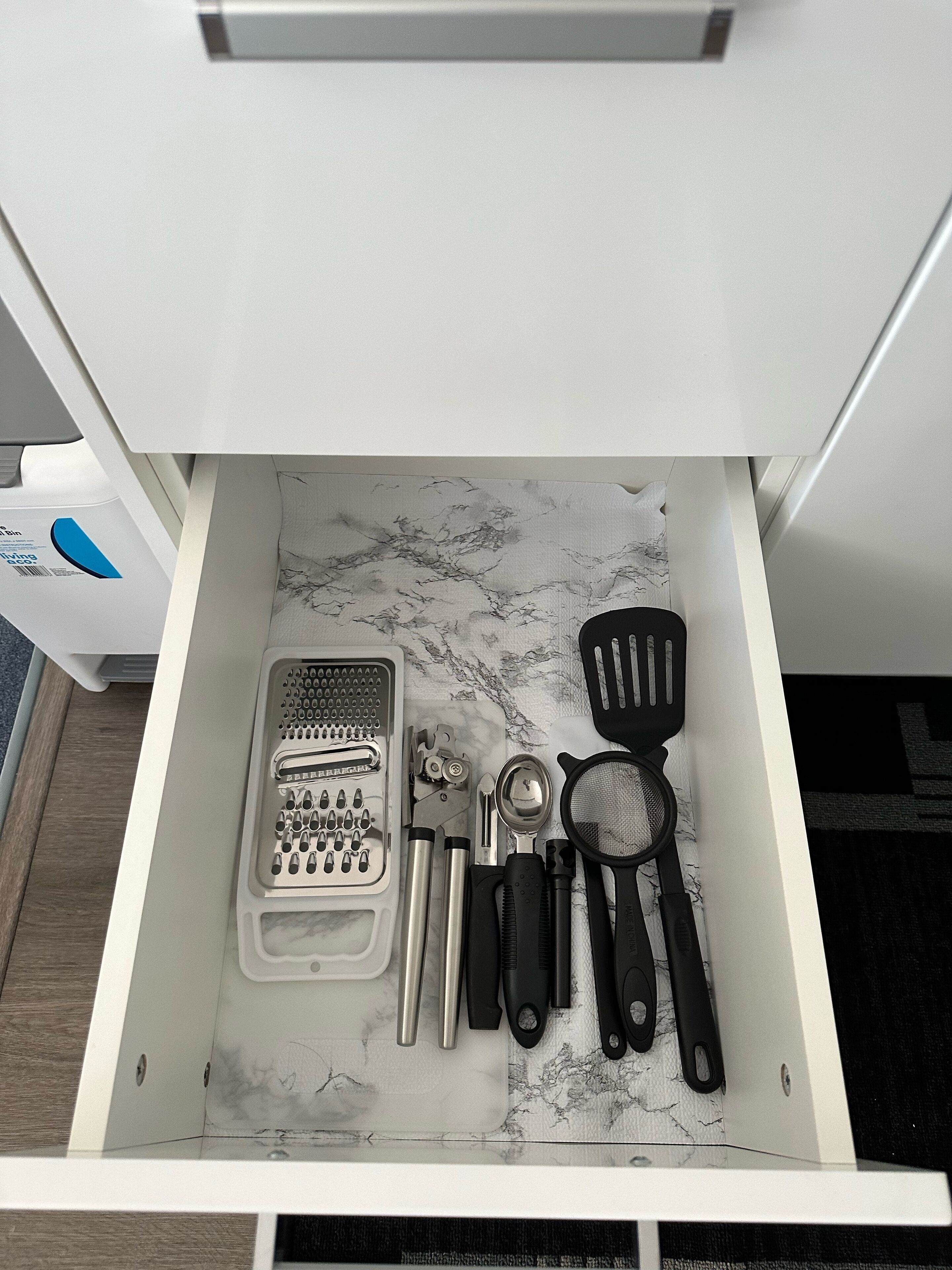 A drawer with kitchen utensils including a grater, spatula, and other tools.
