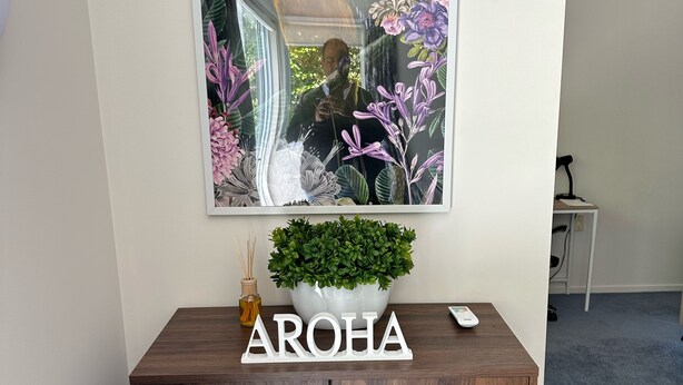 Un mueble de madera con una planta en maceta y un cuadro enmarcado de pájaros y flores en la pared de arriba.