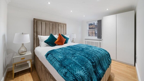 Un dormitorio con cama, mesitas de noche, ventana y armario.