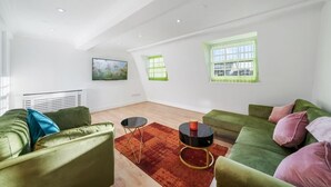 Amplia sala de estar con sofás verdes, una mesa de centro redonda y un cuadro en la pared.