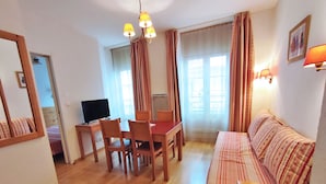 A cozy living room with a wooden dining table, chairs, a sofa, a TV, and a mirror. - Appartement T2 Centre Luchon-wifi - Vacances et Cure - à 280m de la Télécabine (Bagnères-de-Luchon)