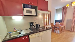 A compact kitchen with a microwave, coffee maker, and dishwasher. There is a dining area with a table and chairs. - Appartement T2 Centre Luchon-wifi - Vacances et Cure - à 280m de la Télécabine (Bagnères-de-Luchon)