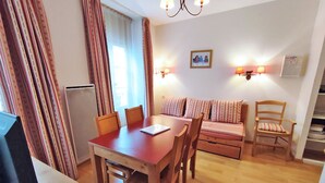 A cozy room with a wooden dining table, chairs, a sofa, and a TV. - Appartement T2 Centre Luchon-wifi - Vacances et Cure - à 280m de la Télécabine (Bagnères-de-Luchon)
