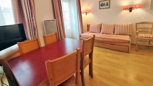 A cozy living room with a wooden dining table, a sofa, and a television. - Appartement T2 Centre Luchon-wifi - Vacances et Cure - à 280m de la Télécabine (Bagnères-de-Luchon)