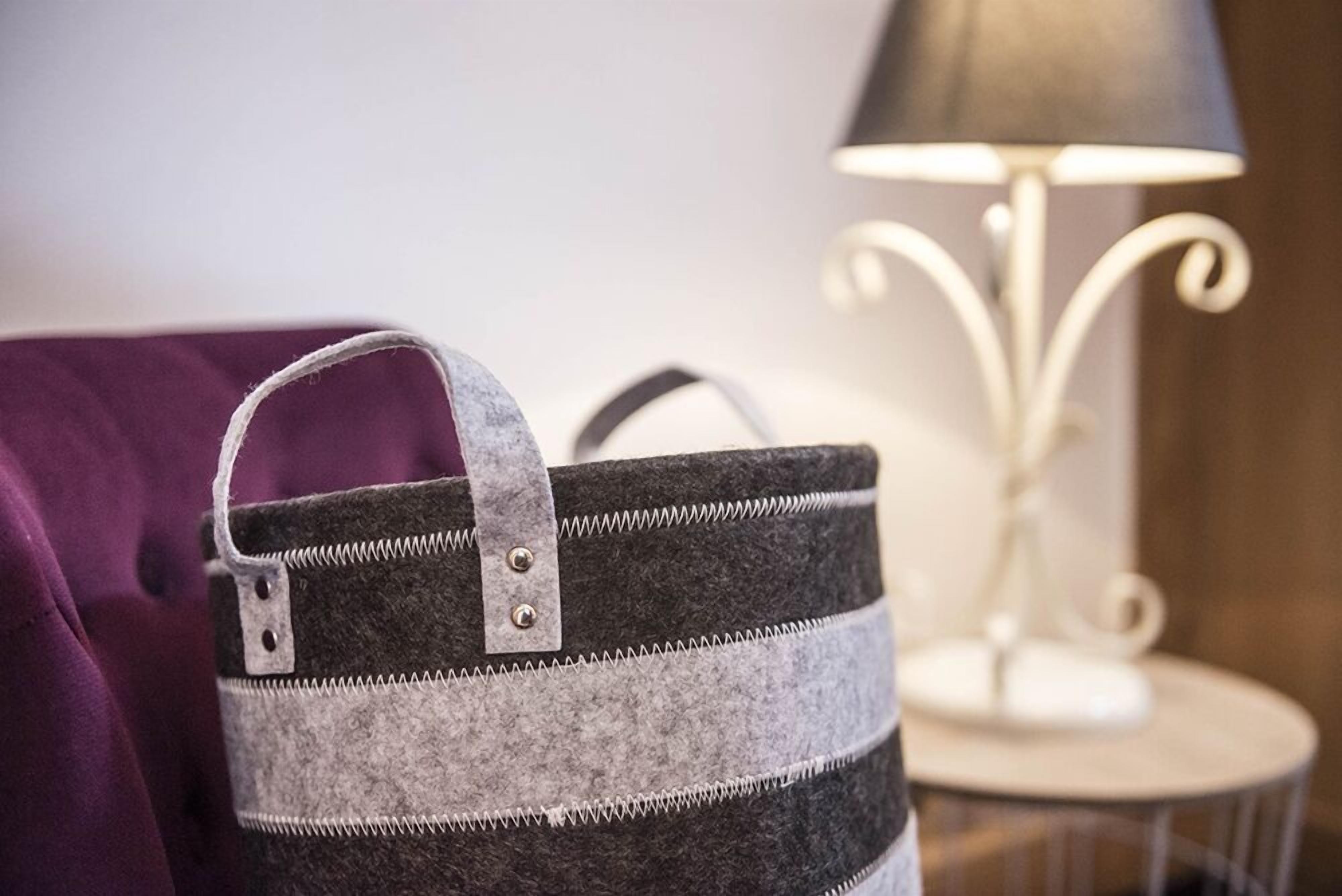 Un bolso a rayas grises y negras con una hebilla metálica y un asa, sobre un sofá morado.