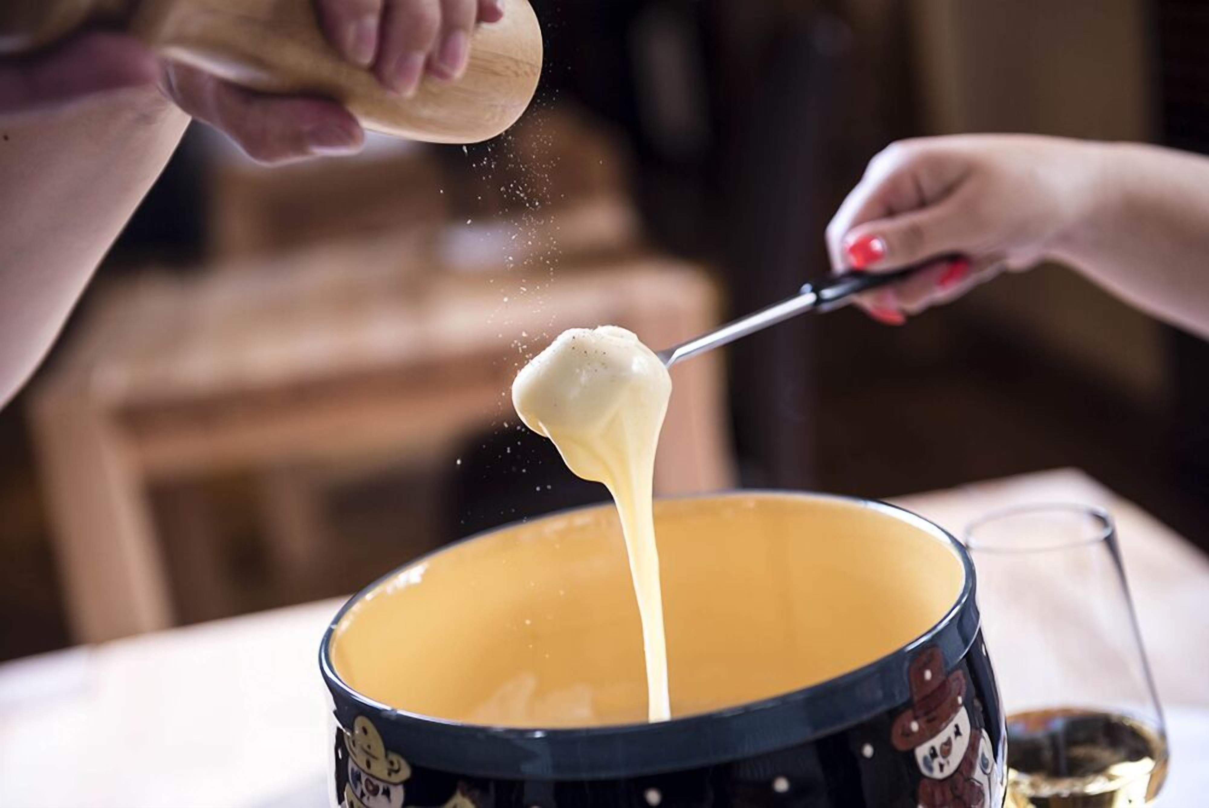 A person stirring a pot of melted cheese.