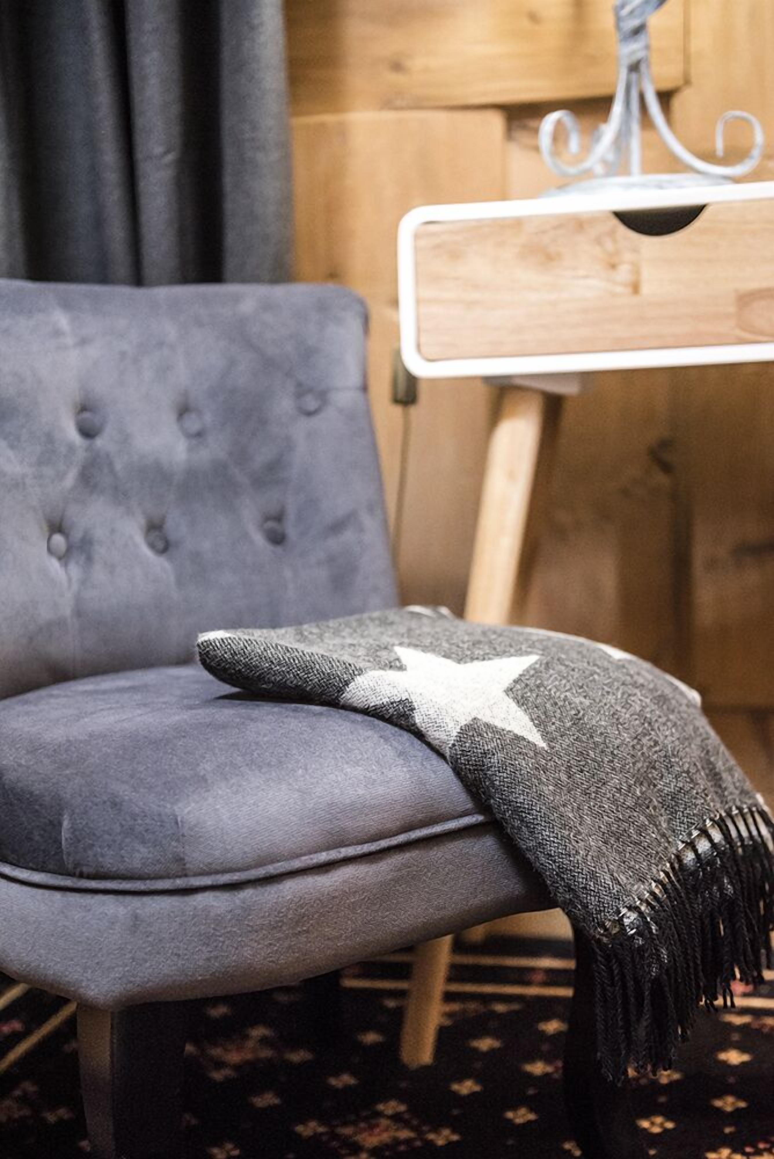 Un fauteuil gris recouvert de tissu, agrémenté d’un plaid à motifs étoilés.