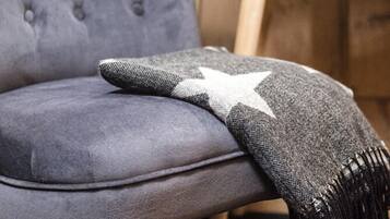 Un fauteuil gris recouvert de tissu, agrémenté d’un plaid à motifs étoilés.
