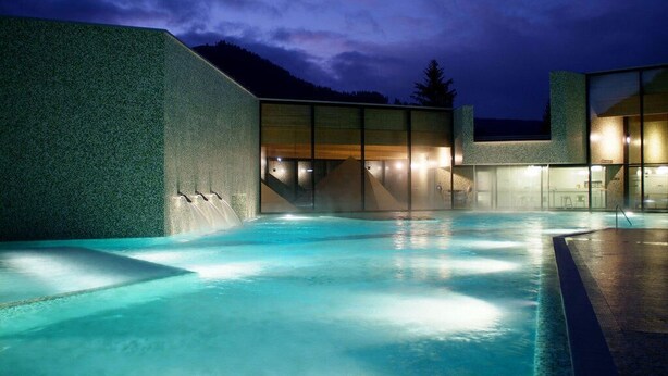 A modern building with a pool area, large windows, and a view of the mountains.