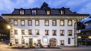 A white building with multiple windows, a sign reading "HOTEL DE L'ETOILE," and a string of lights above the entrance.
