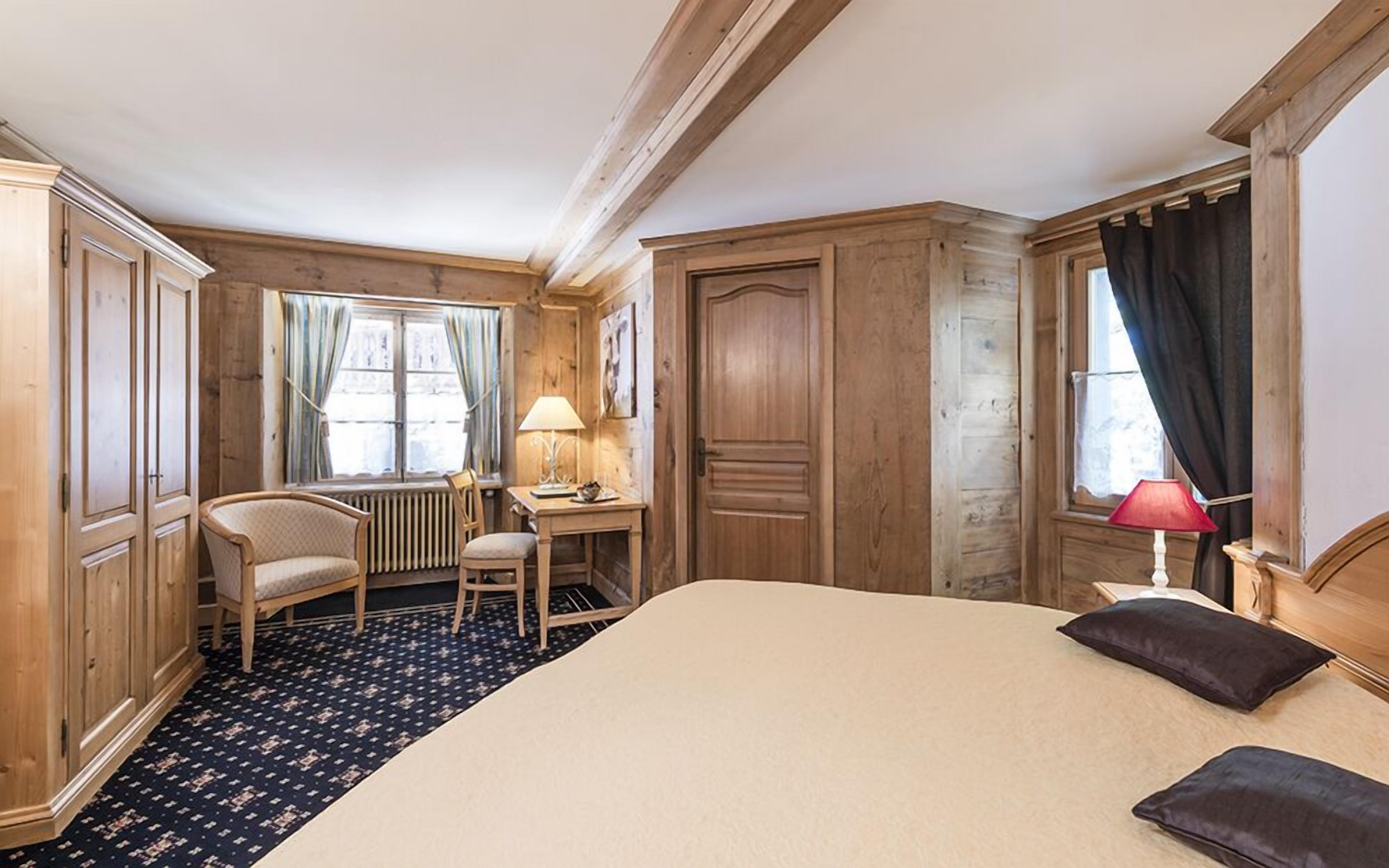 A hotel room with a large bed, a desk with a chair, a radiator, and wooden paneling.